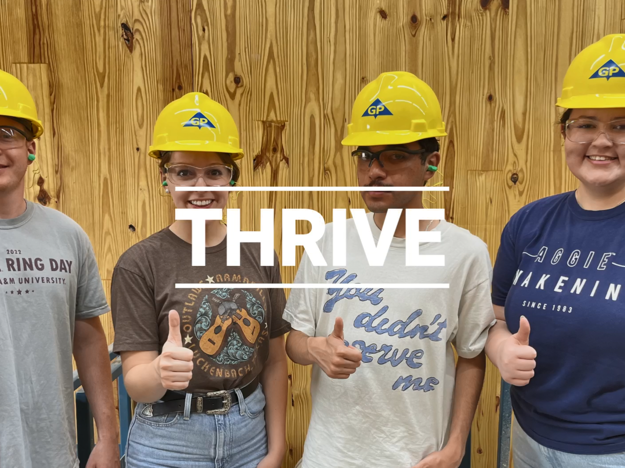 Four people giving thumbs-up, wearing matching yellow hard hats. "Thrive" on top of the image.