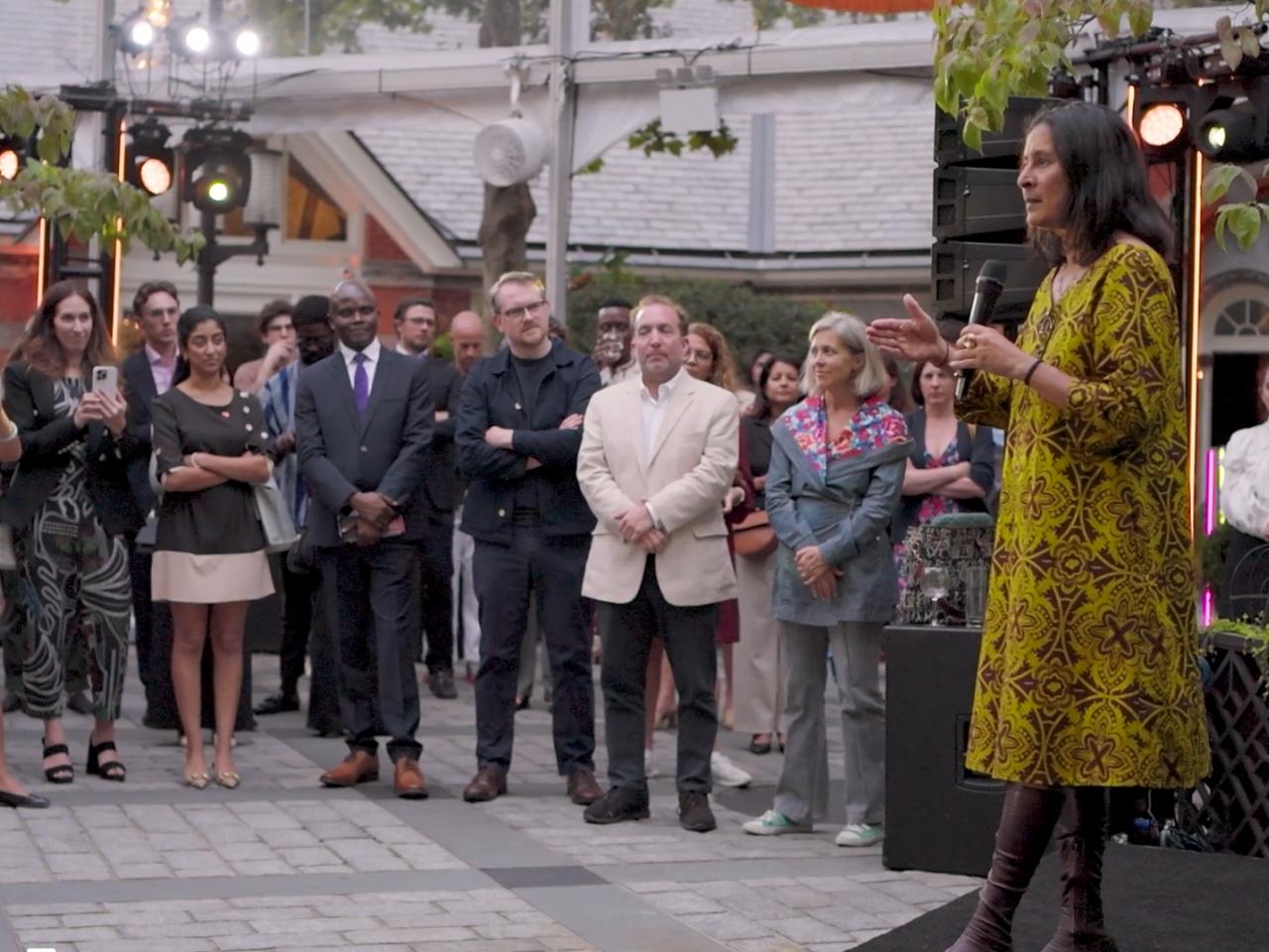 Someone with a microphone, speaking to a small crowd outside