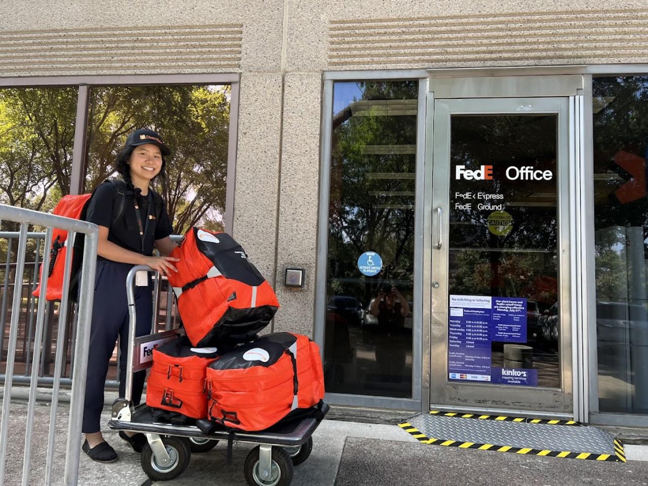 Someone rolling red bags on a trolley to a FedEx office
