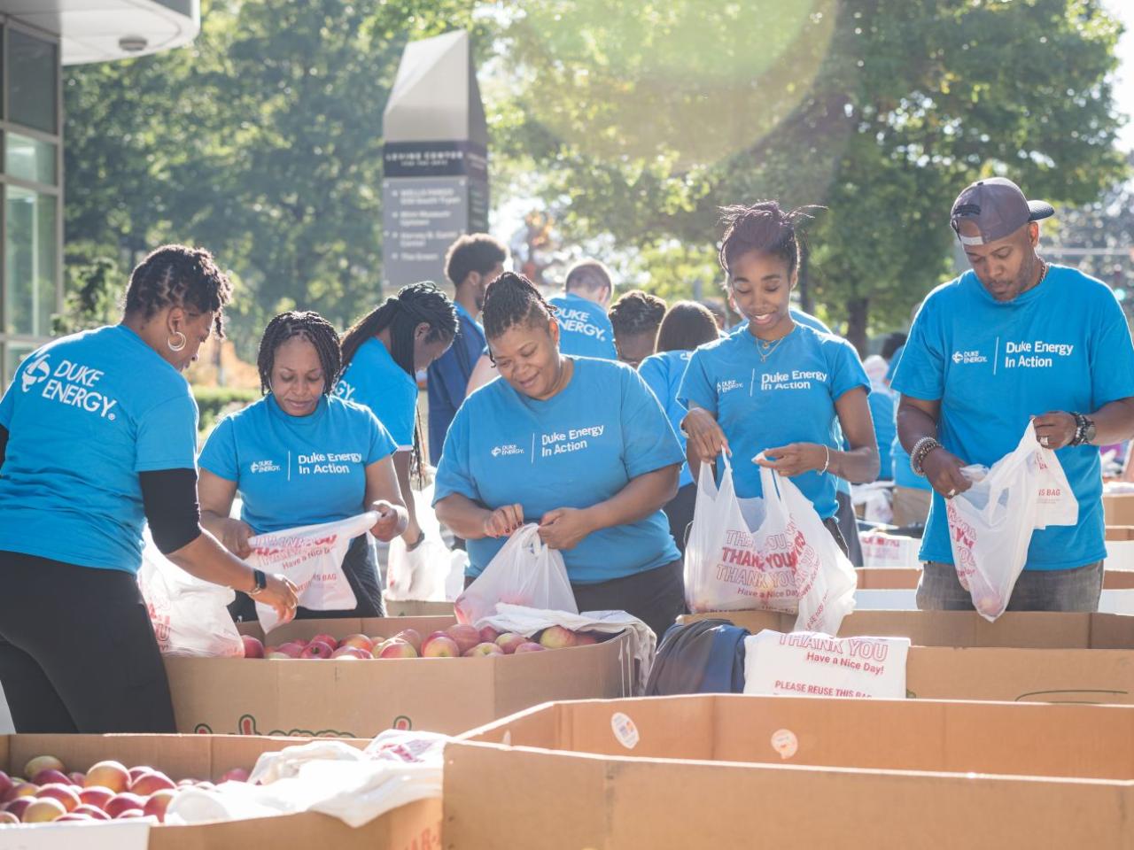 Volunteers packing bags with produce items in large bins outside.