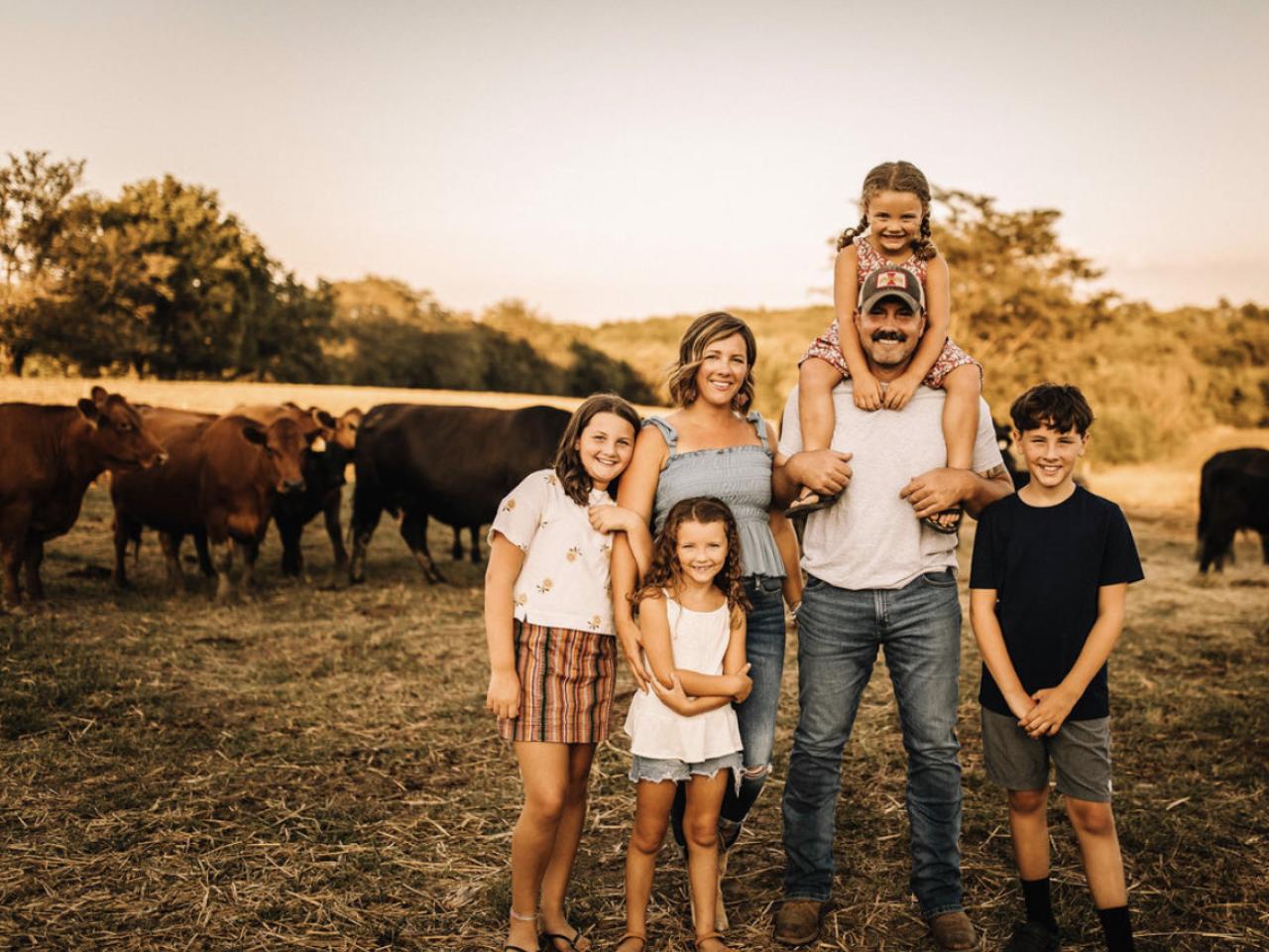 A family posed standing in a field in front of cows.