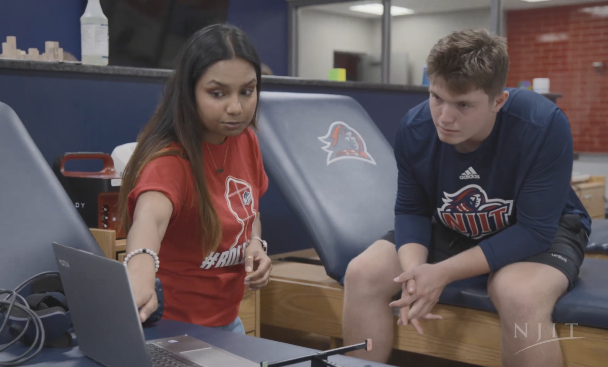 A student pointing at a laptop as another looks on from a physical therapy-type seat/bench.