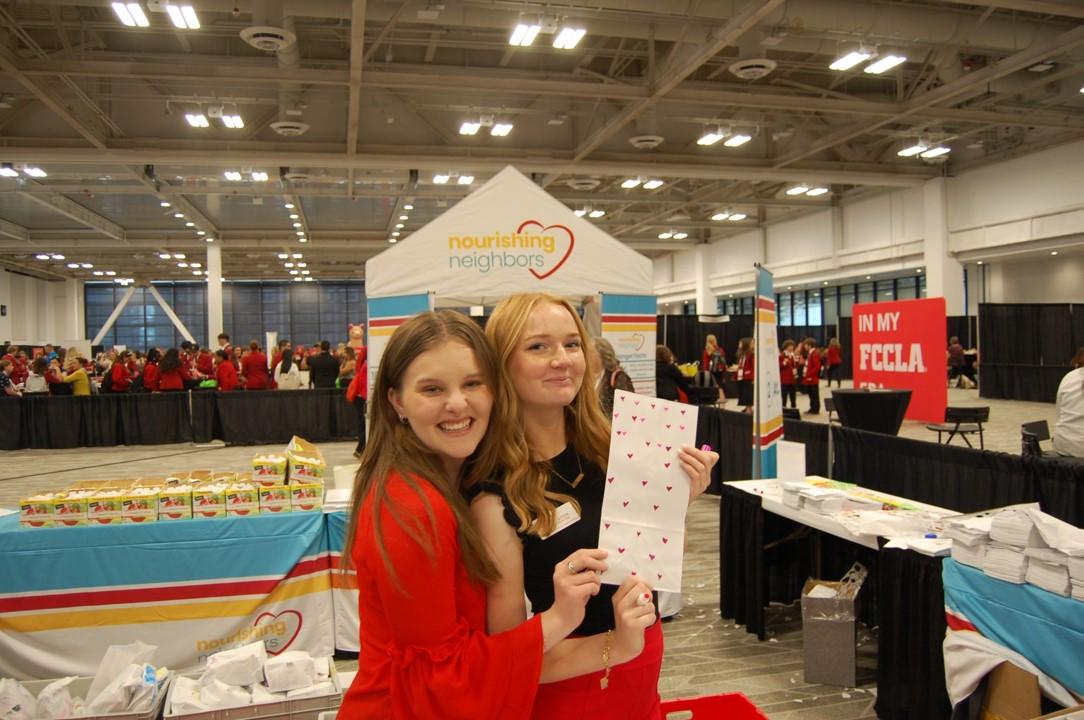 Two people posing in front of Nourishing Neighbors booth