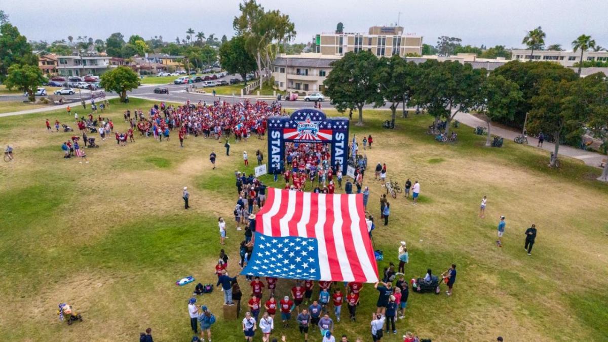 People holding a large American flag on a field  