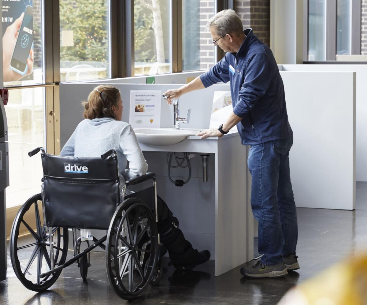 Woman in wheelchair being shown an accessible sink by a standing man