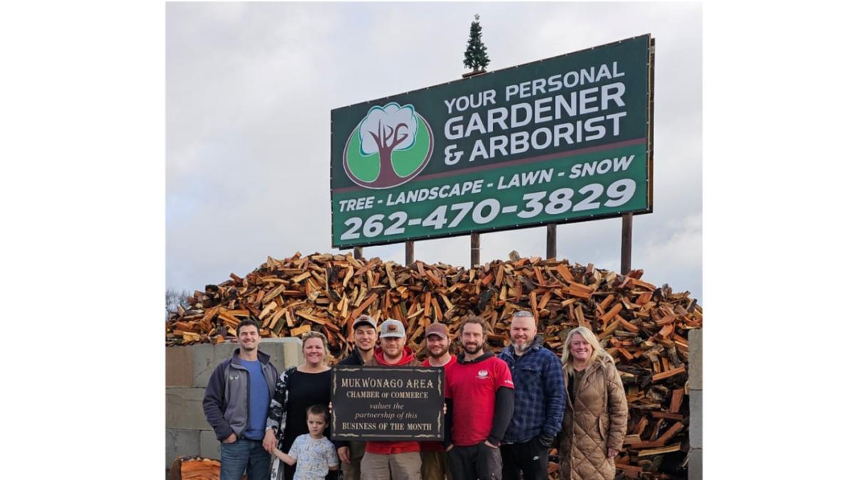 A group of people posing in front of a sign: "Your Personal Gardener & Arborist"