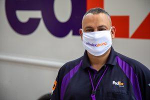 Employee in uniform stands in front of FedEx truck, wearing a mask that says #fedex strong