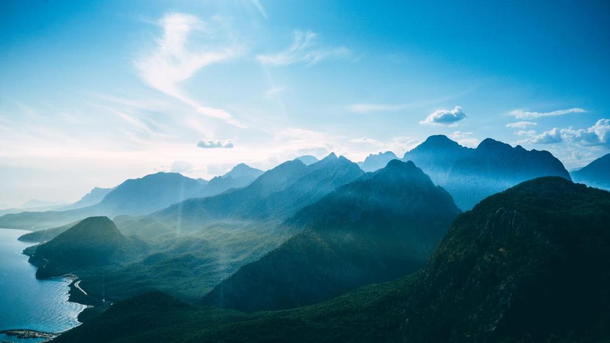 Aerial view of mountain landscape and slightly clouded blue sky.