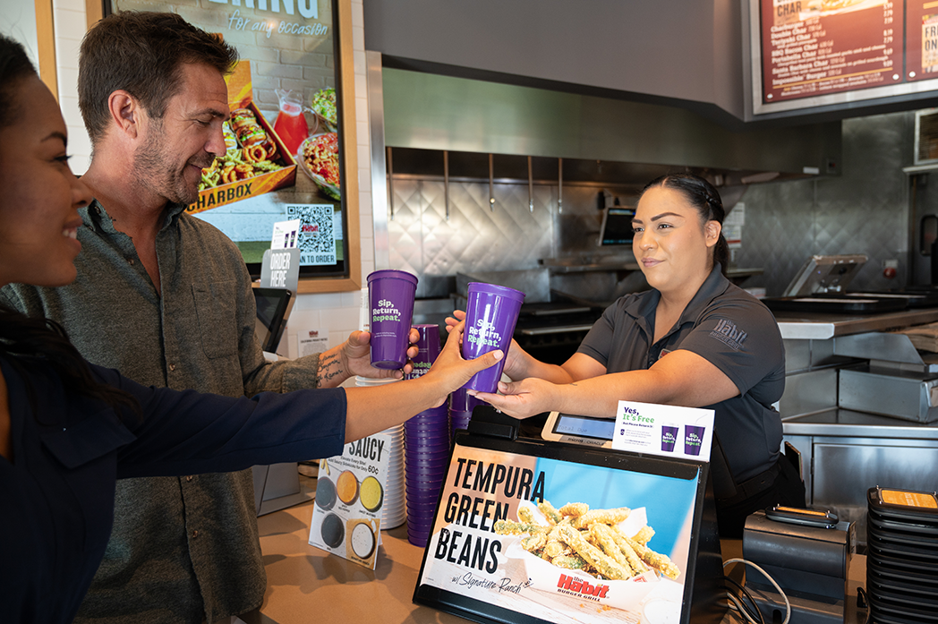 A restaurant worker handing reusable purple cups to customers