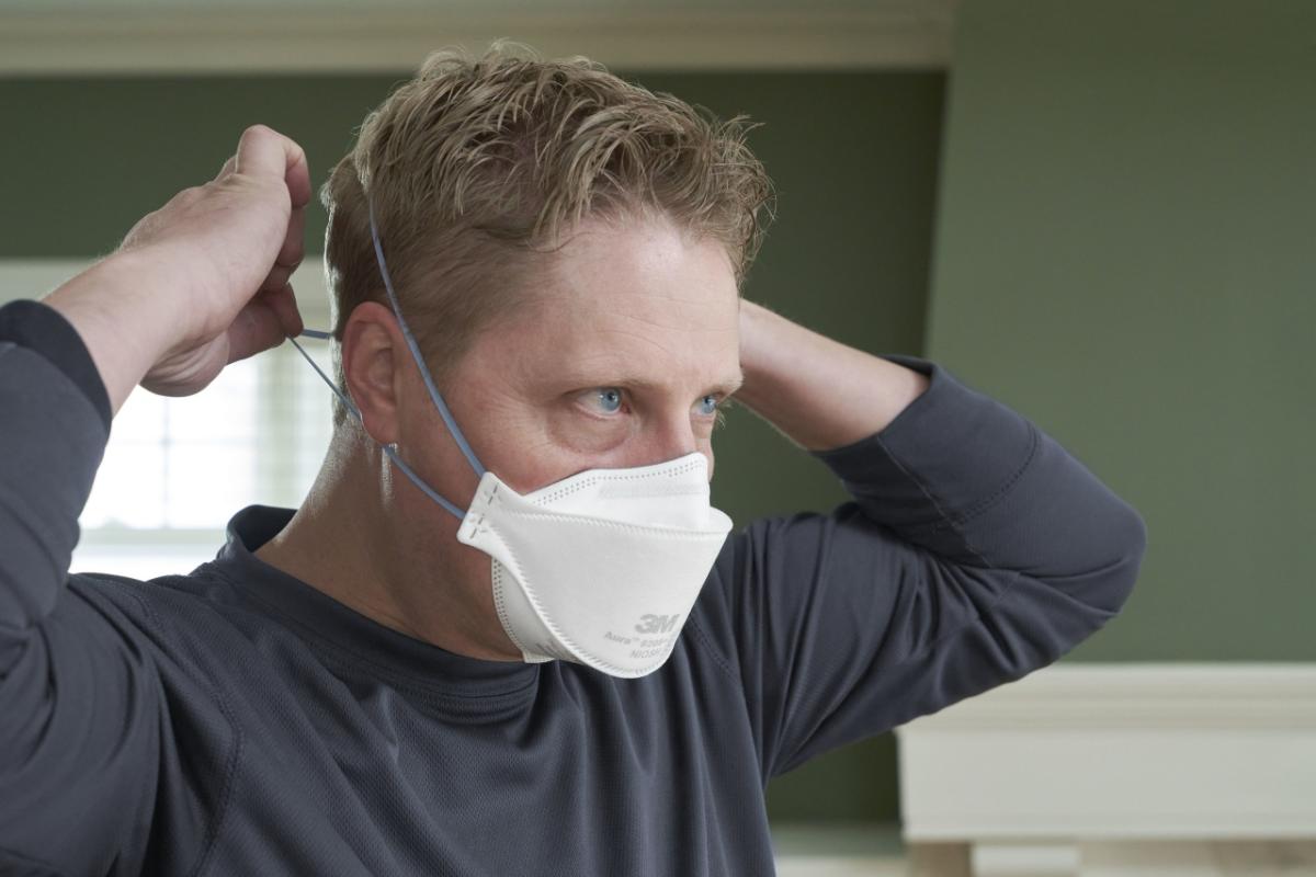 Male showing how to properly fit N95 mask and secure the back.