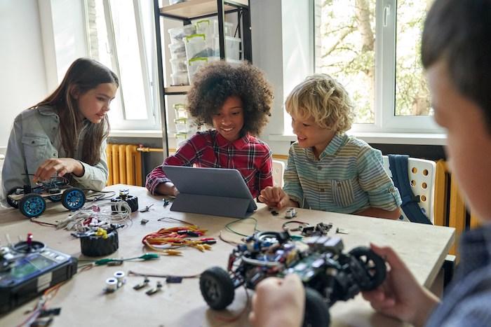 Four students are seated at a table behind a laptop and with science experiments in front of them.