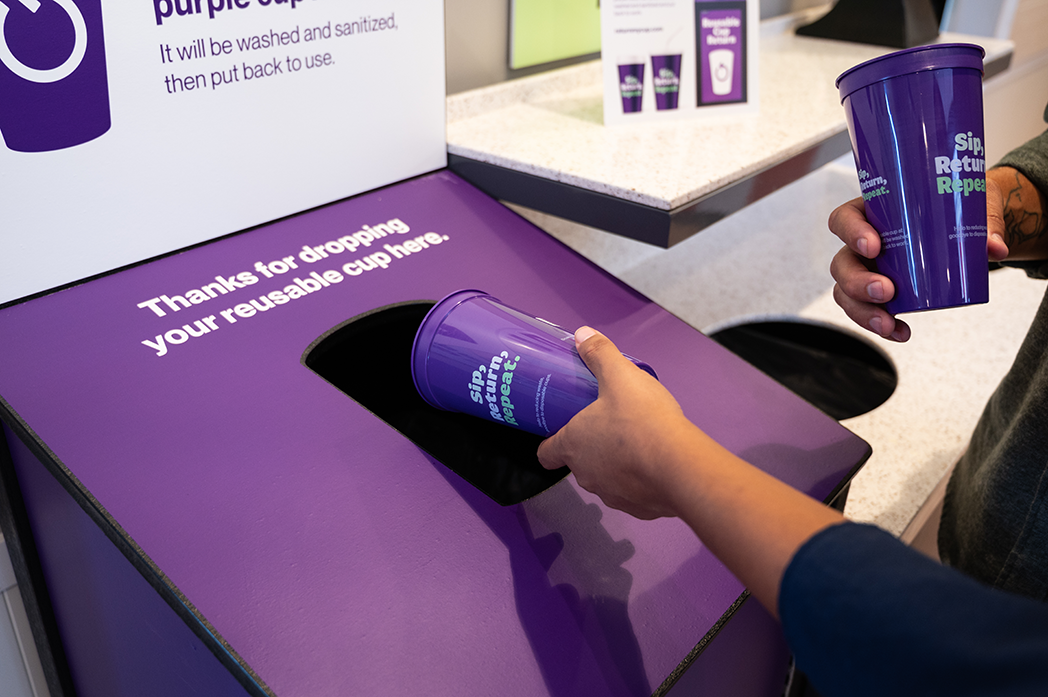 Someone dropping a reusable purple cup into a bin