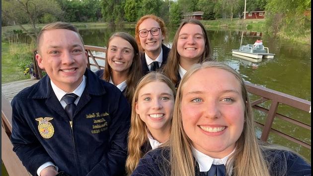 Kids posed in a group selfie on a pier over a small body of water.