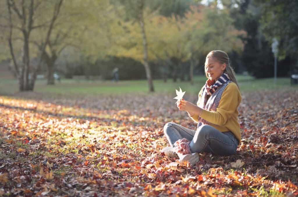 Young woman seated in a park in the fall holding a leave.