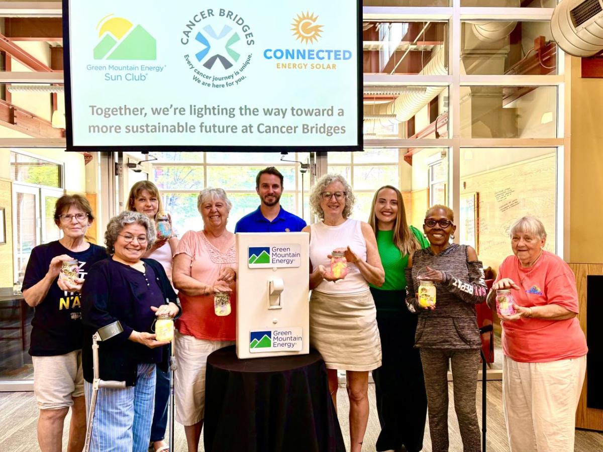 Members from Cancer Bridges, Connected Energy Solar, and Green Mountain Energy Sun Club smiling with solar mason jars and a life-size light switch.