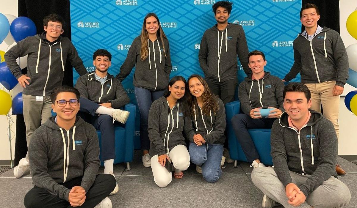interns in gray hoodies pose in front of a blue applied materials logo wall
