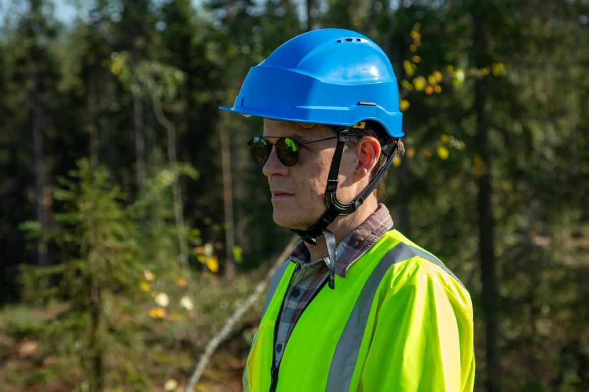 John Mulcahy in hard hat and high-vis clothing standing in a forested area.