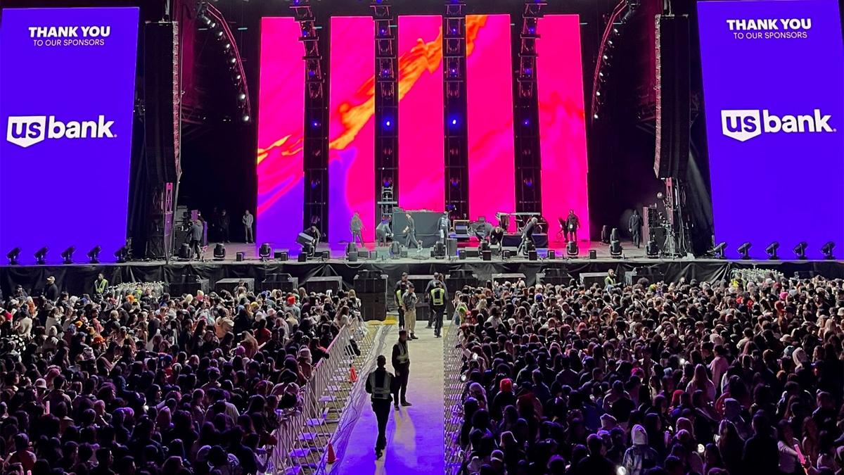 A large performance stage with digital screens, a large seated audience, and ushers in the aisle.