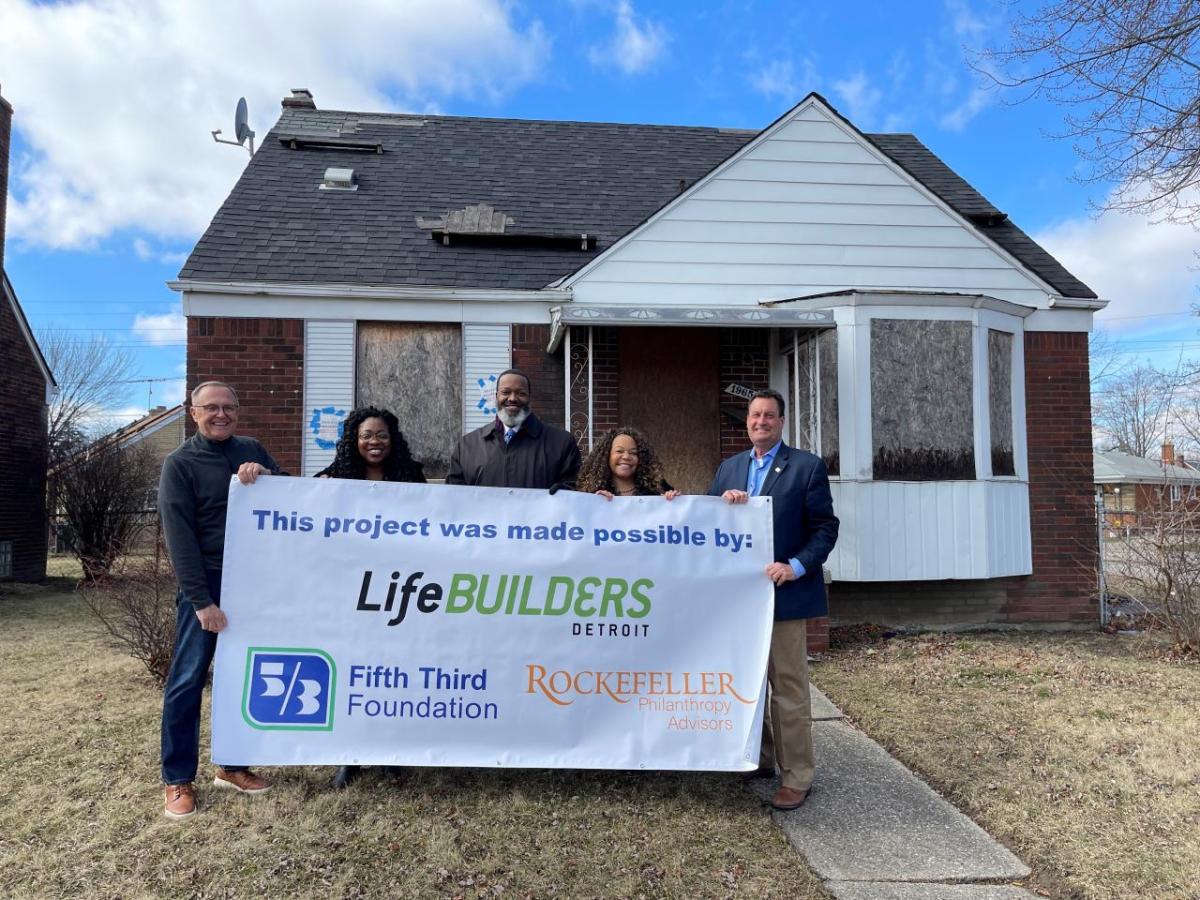 5 people holding a LifeBUILDERS sign outside a house