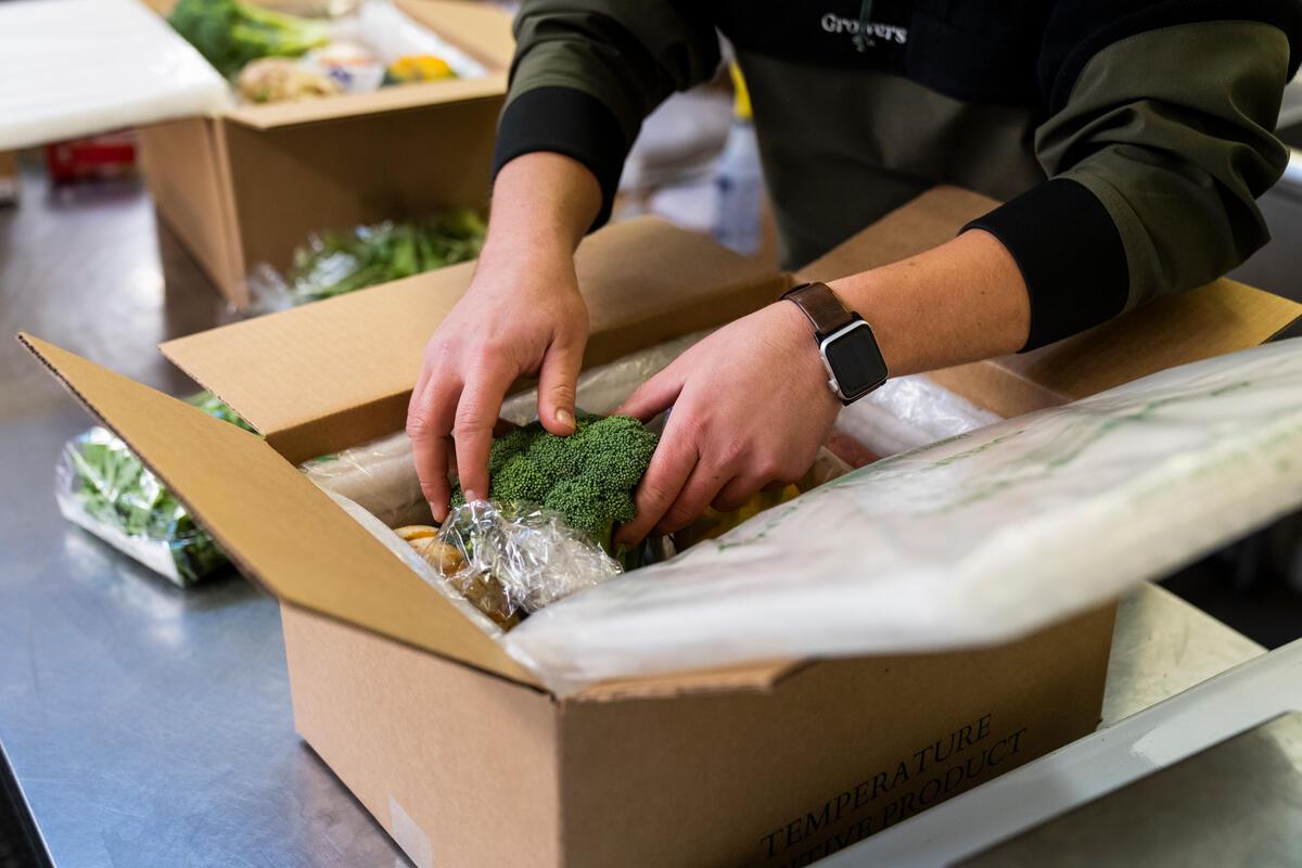 person packs vegetables into a box