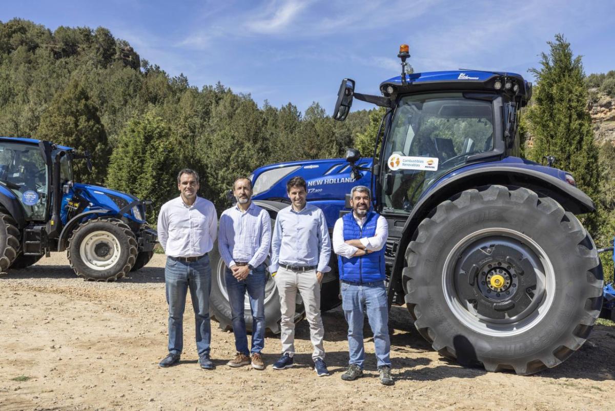 Four people outside standing in front of a new holland tractor