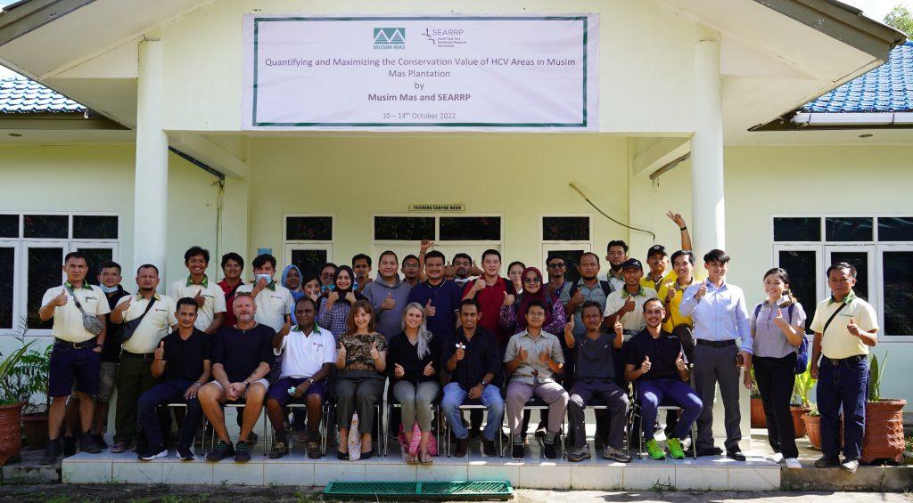 A large group of people together in front of a building under a banner "Musim Mas and SEARRP."