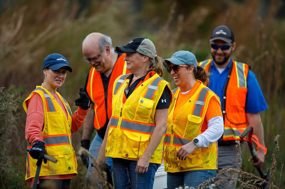 5 people laughing. They are outside, wearing high-vis vests and work wear.