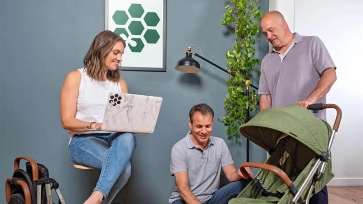 A person sat on a stool while two other people look at a pushchair  