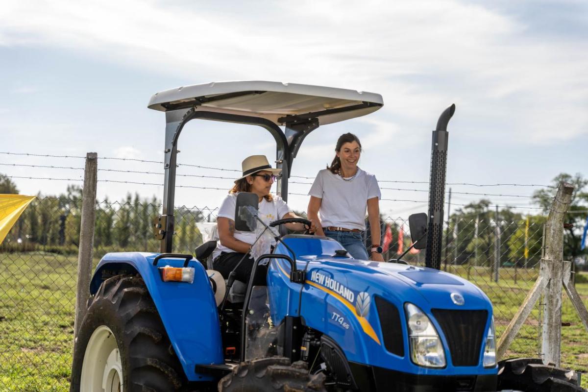 One person sat in a blue tractor with another person stood at the side