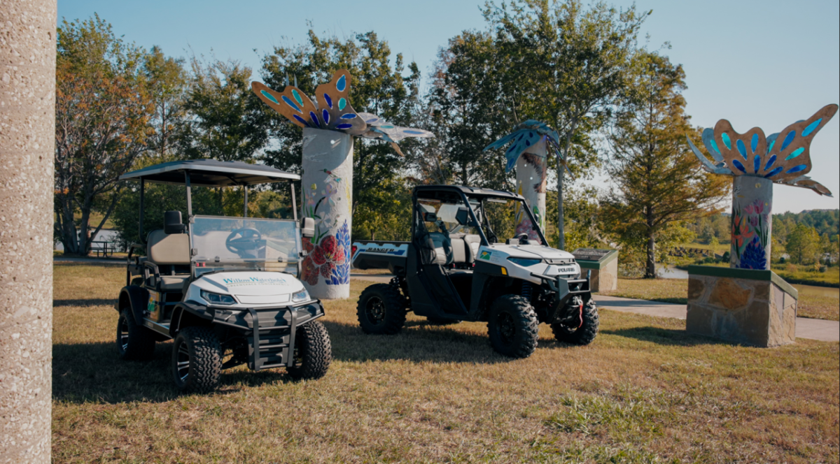 Two UTVs are parked in a grassy sunny area.