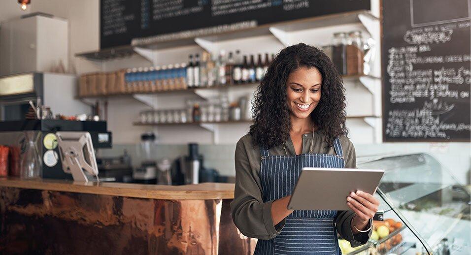 A smiling person works on a tablet device in a cafe setting.