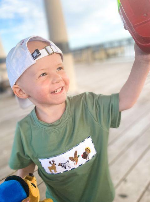 Cole smiling, holding up toys outside.