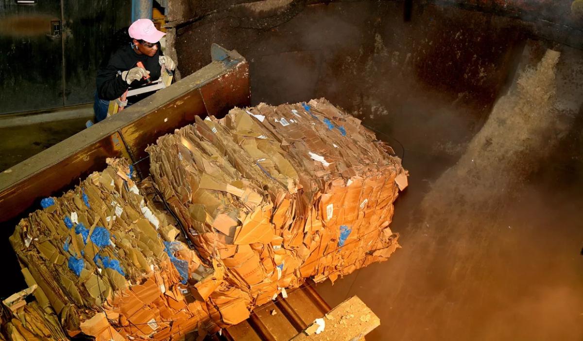 A person watchin as bales of compressed paper travels on a conveyor to a collection pit.