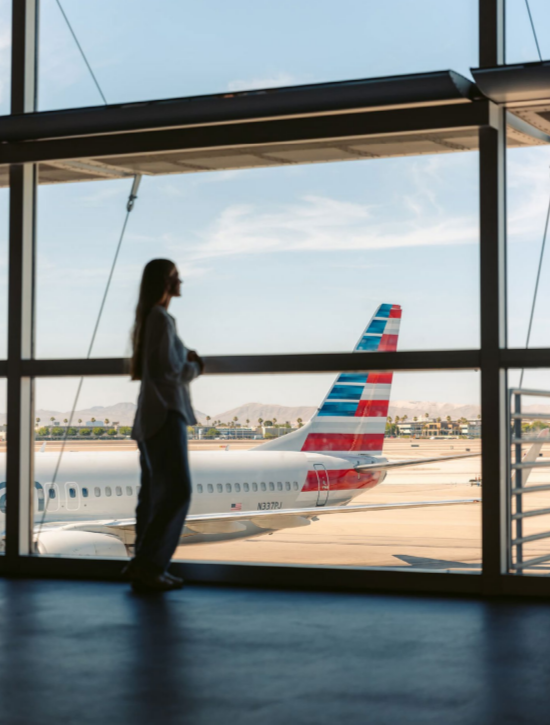 A person, standing, looking out a large window at planes parked outside.