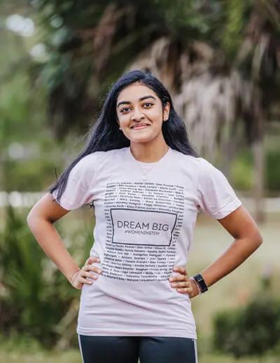 A person smiling at the camera, hands on their hips. Wearing a "dream big" t-shirt. 