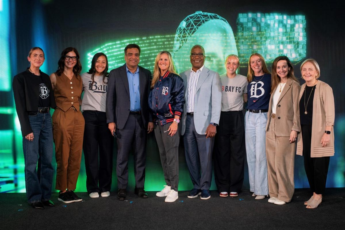 A standing group of people posed together in front of a dark screen with bright green digital symbols.