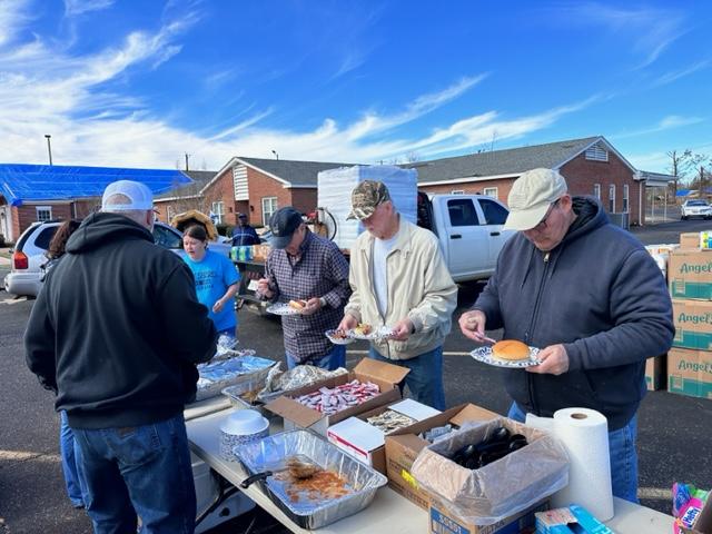 People in line assembling food plates in a parking lot.