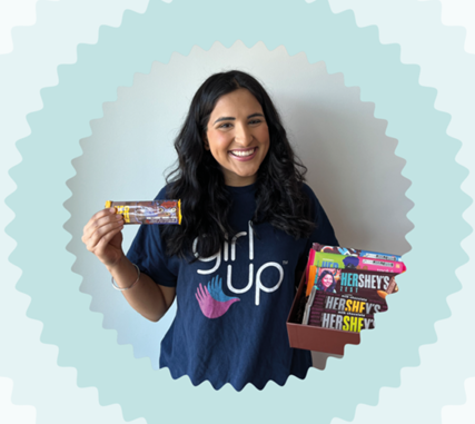 A smiling person wearing a "Girl up" t-shirt, holding up a Hershey bar.