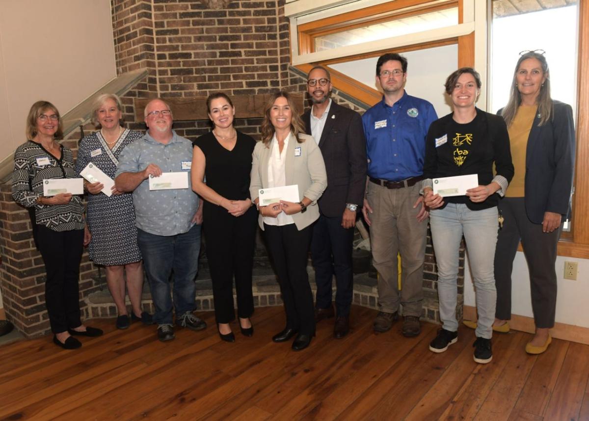 A group posed in front of a fireplace, many holding checks.