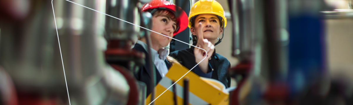 Two people in hard hats in the midst of industrial equipment and piping.
