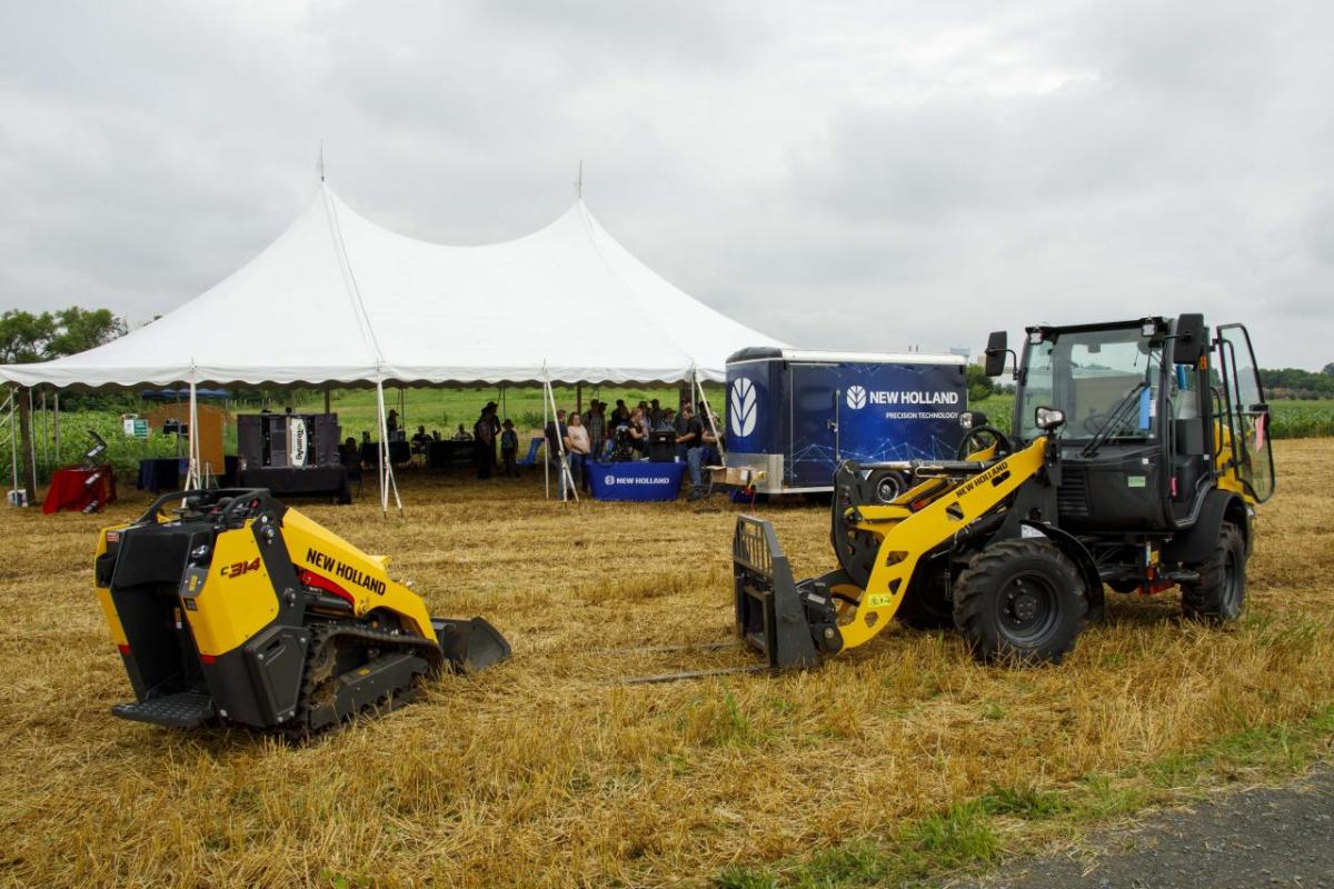 two yellow tractors outside with a tent in the background