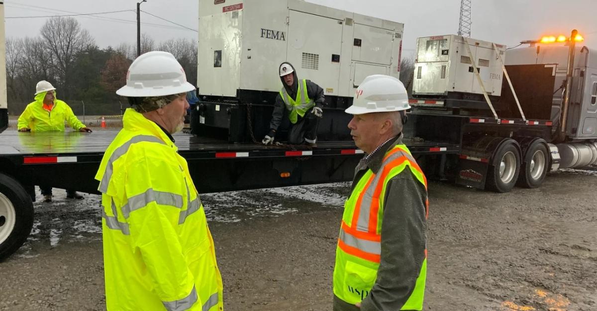 two workers outside stand beside a large trailer where two others are standing near a large generator on the trailer