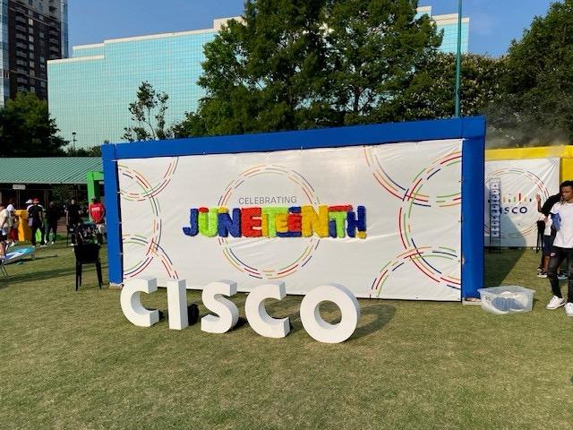 An outdoor sign "Juneteenth" behind CISCO lettering on a grassy area.