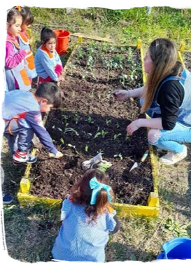 an adult crouched by a garden bed, children surrounding it