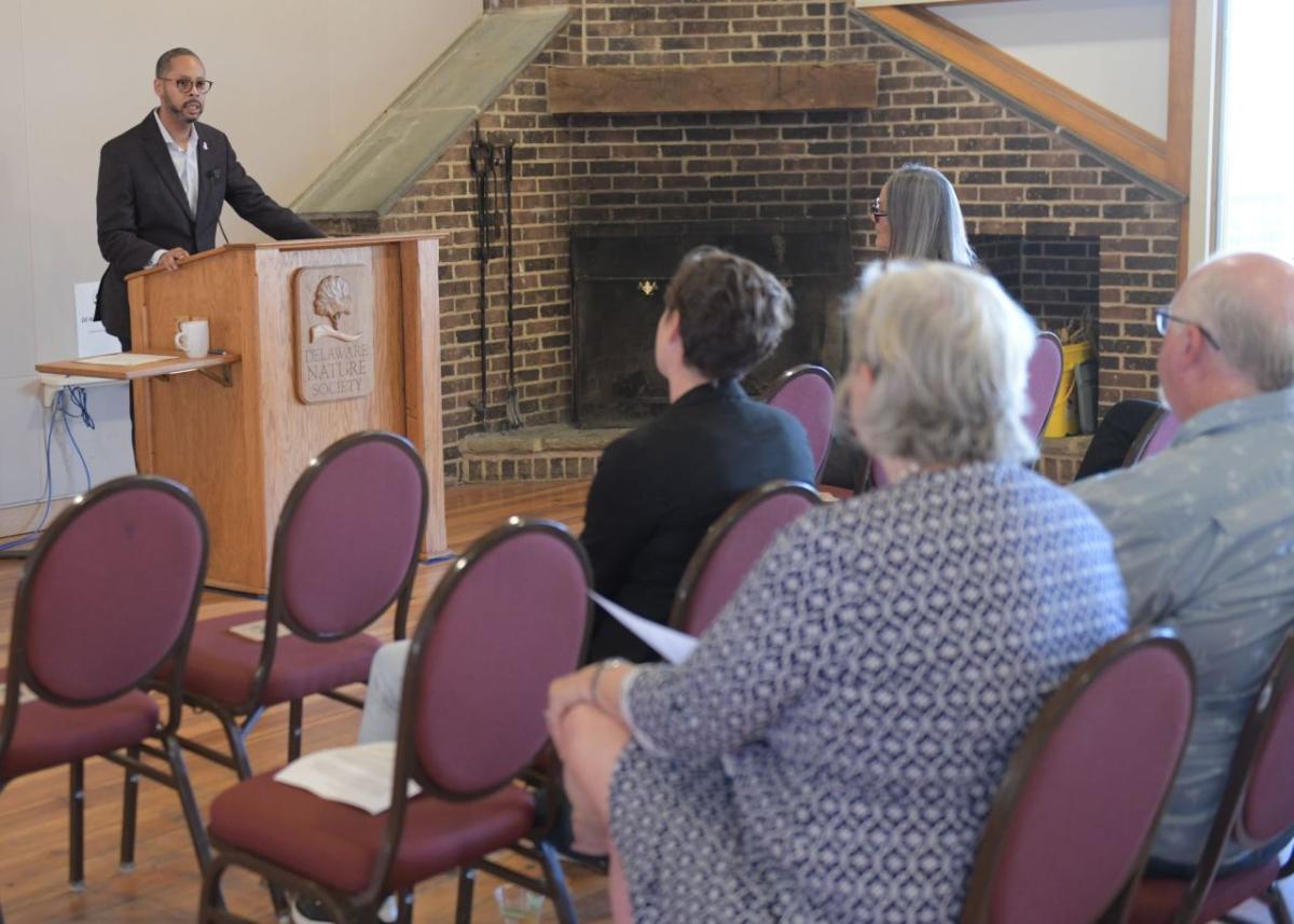 A person speaking at a podium in a room of others seated.