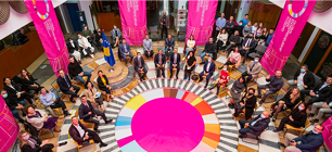 aerial shot of a large group of people sitting around a pink circle in a rotunda. Banners hanging from the second floor.
