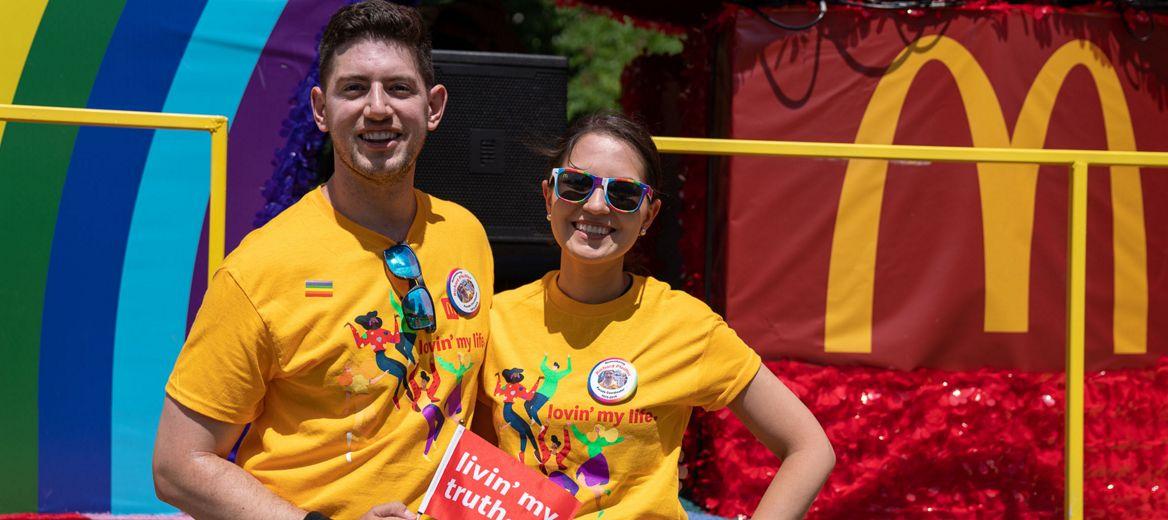 Two people in matching shirts. McDonalds logo and part of a rainbow behind them.