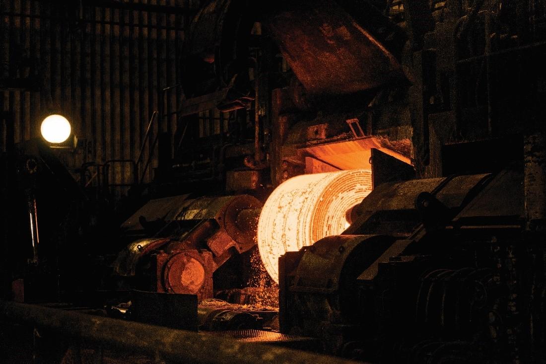 Large steel coil being formed just out of the furnace glows in a dark foundry