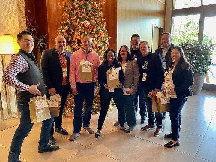 Blanca and a group of other staff each holding a bag in front of a christmas tree