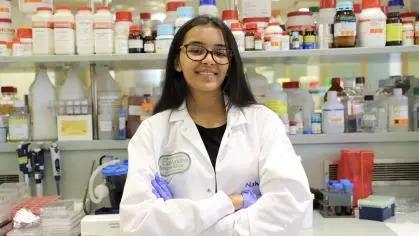 A smiling student in protective lab gear posed with arms crossed in a lab setting